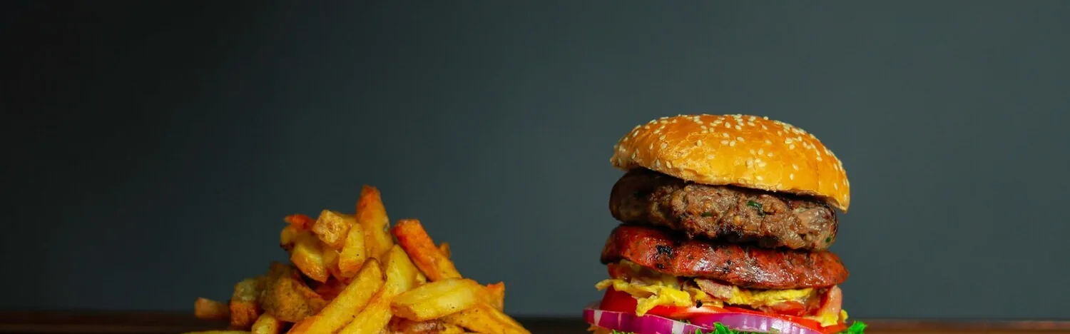 Tall double burger in a sesame seed bun with a pile of french fries beside it.