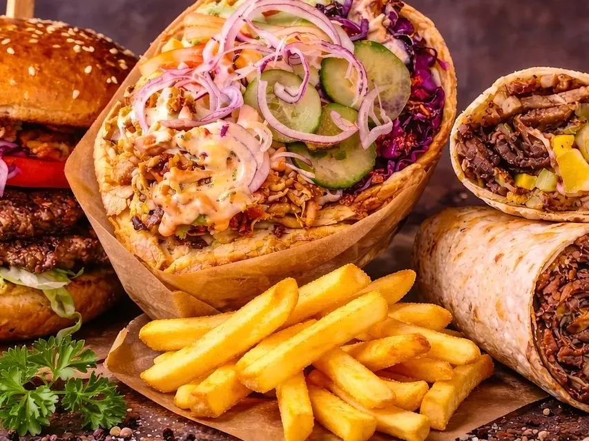 A loaded wrap topped with cucumber and red onion beside burgers, other wraps, and French fries.