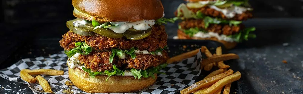 Crispy chicken burgers with lettuce, pickles and mayonnaise, with french fries scattered beside them.