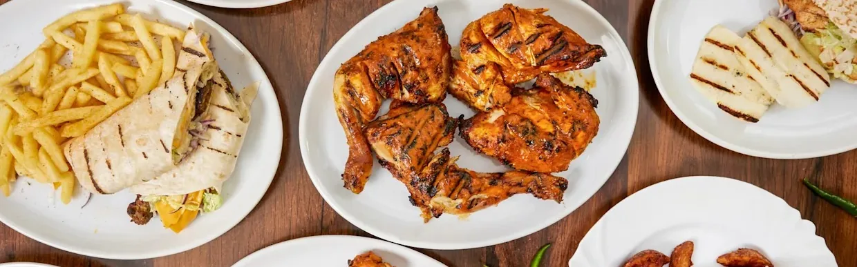 Plates of charred grilled chicken, a wrap with french fries and grilled cheese slices on a wooden table.