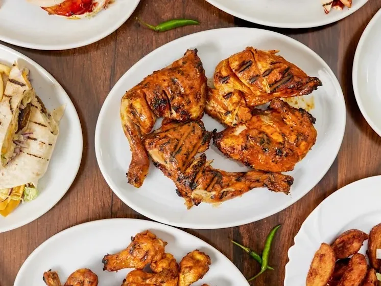 Plates of grilled chicken, chicken wings, and wraps on a wooden table.