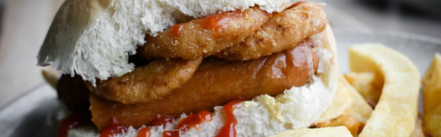 Close-up of a sandwich filled with battered fried strips and ketchup, with thick-cut fries beside it.