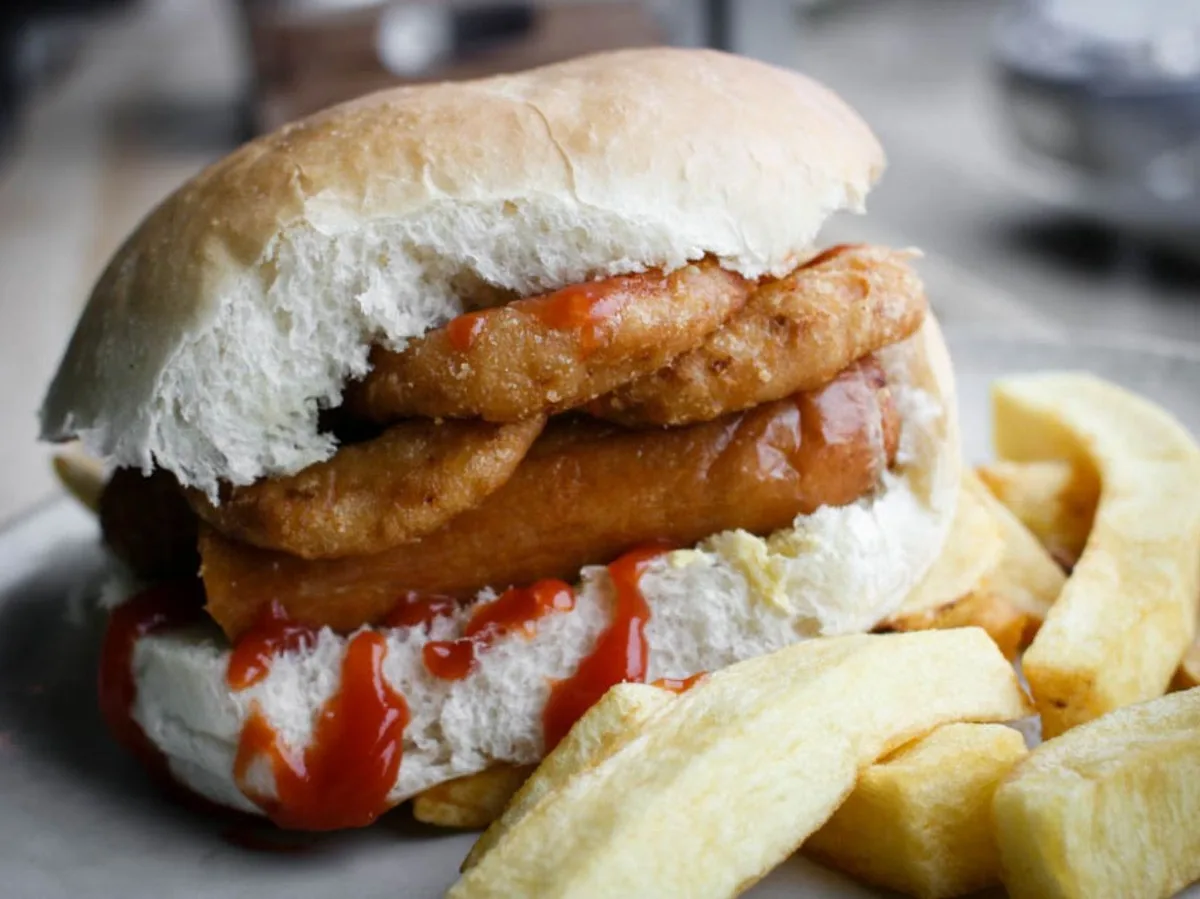 A fried fish sandwich with ketchup in a soft bun, served with thick-cut chips.