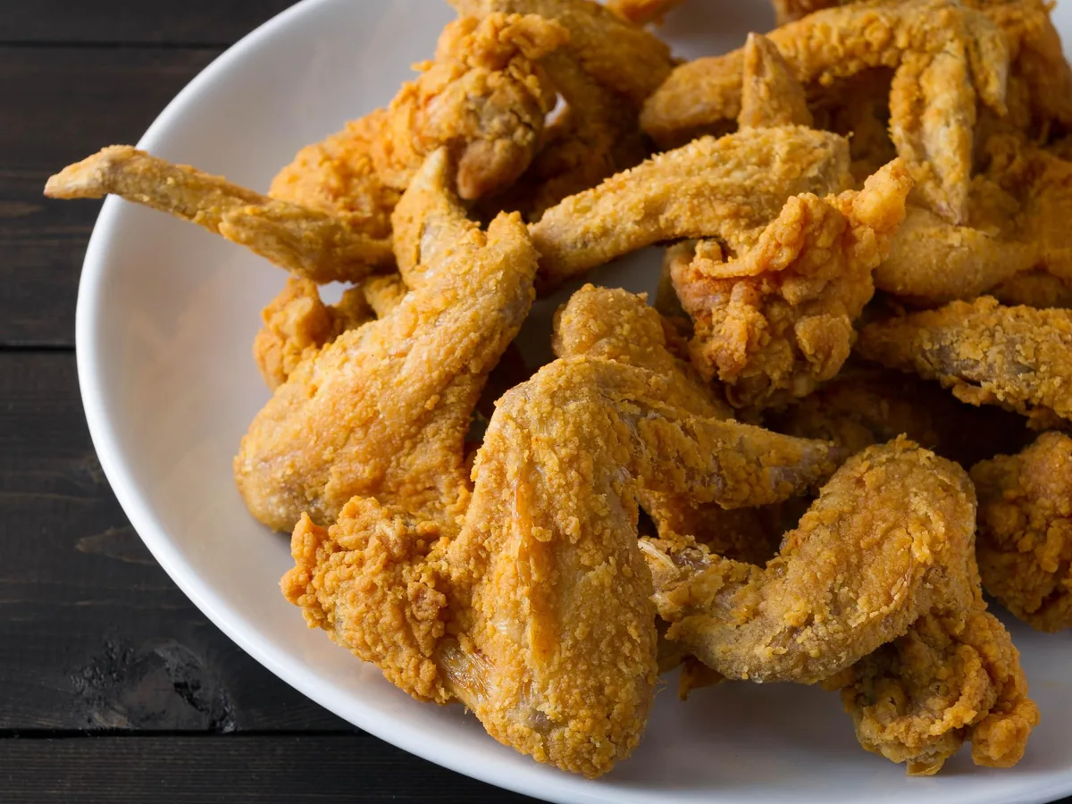 Crispy fried chicken wings piled on a white plate on a dark wooden table.