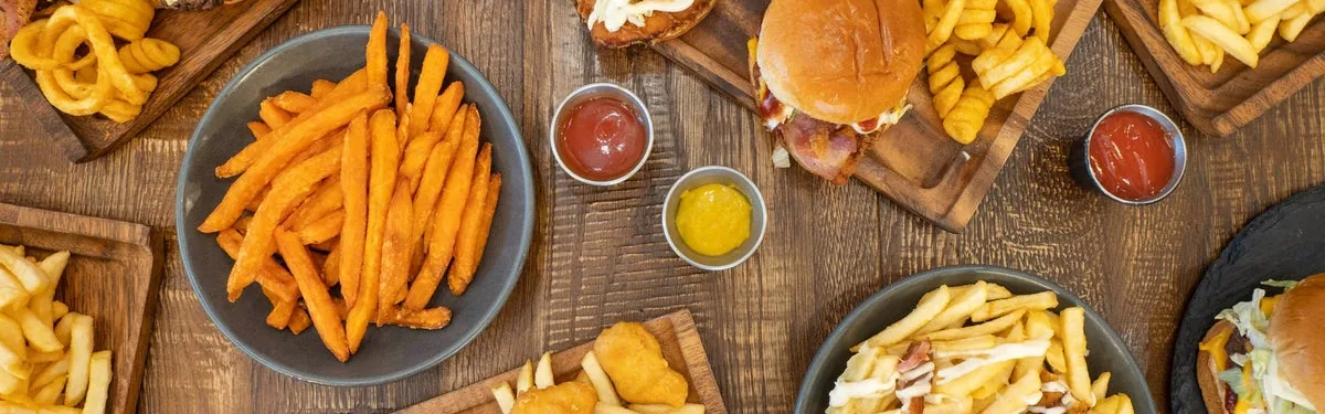 Overhead spread of burgers, french fries, sweet potato fries and dipping sauces on a wooden table.