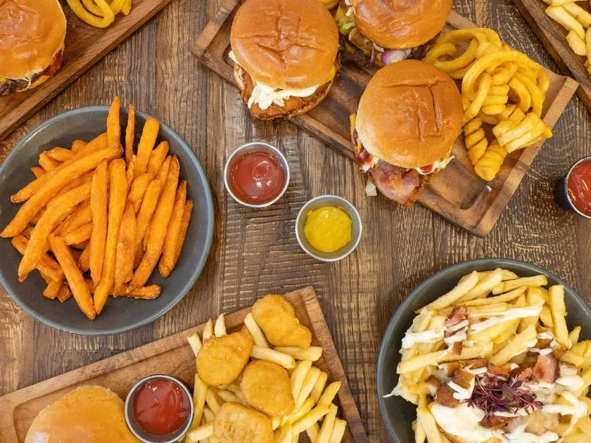 Burgers, curly fries, chicken nuggets and loaded fries with dipping sauces spread across a wooden table.