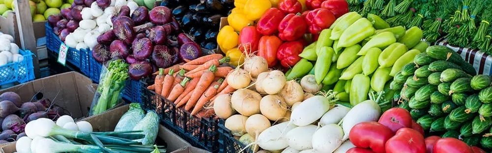 Market stall display of fresh vegetables including onions, carrots, peppers, cucumbers and tomatoes.