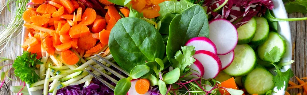 Fresh salad with sliced carrots, cucumber, radishes, spinach leaves and herbs.