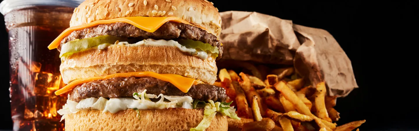 Double cheeseburger with pickles, french fries and a glass of cola on a dark background.