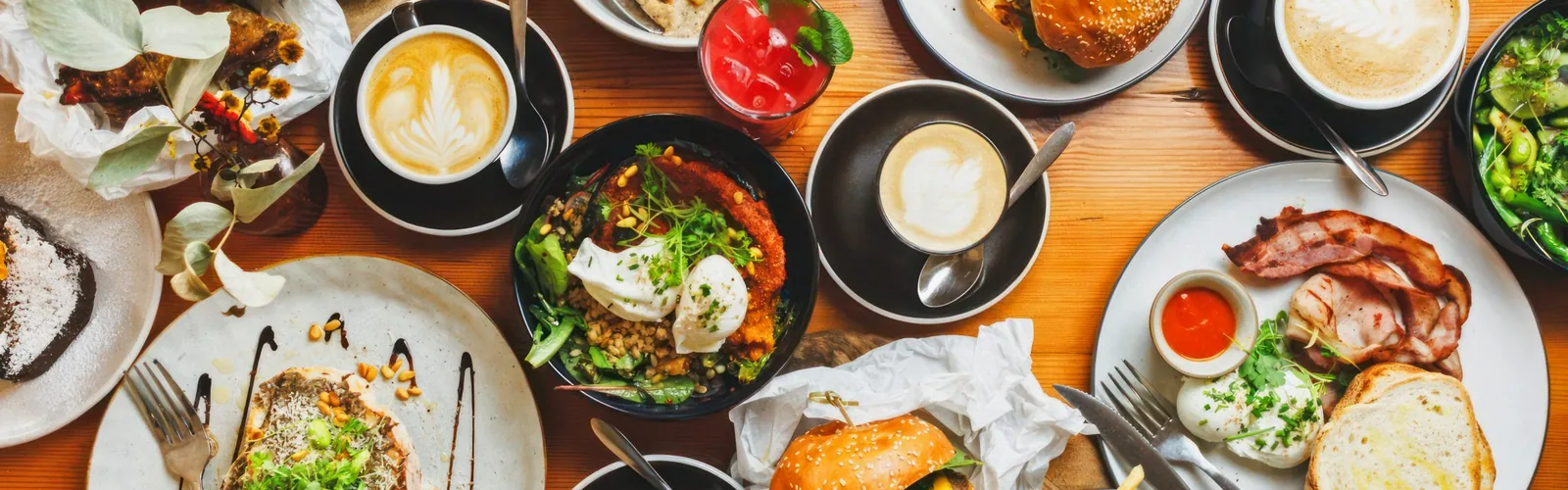 Overhead cafe brunch spread with burgers, coffees and fries