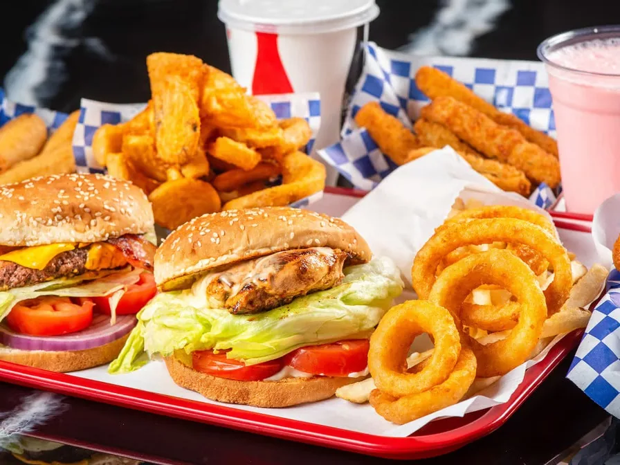 Two burgers with onion rings, fries, chicken strips and drinks arranged on a tray.