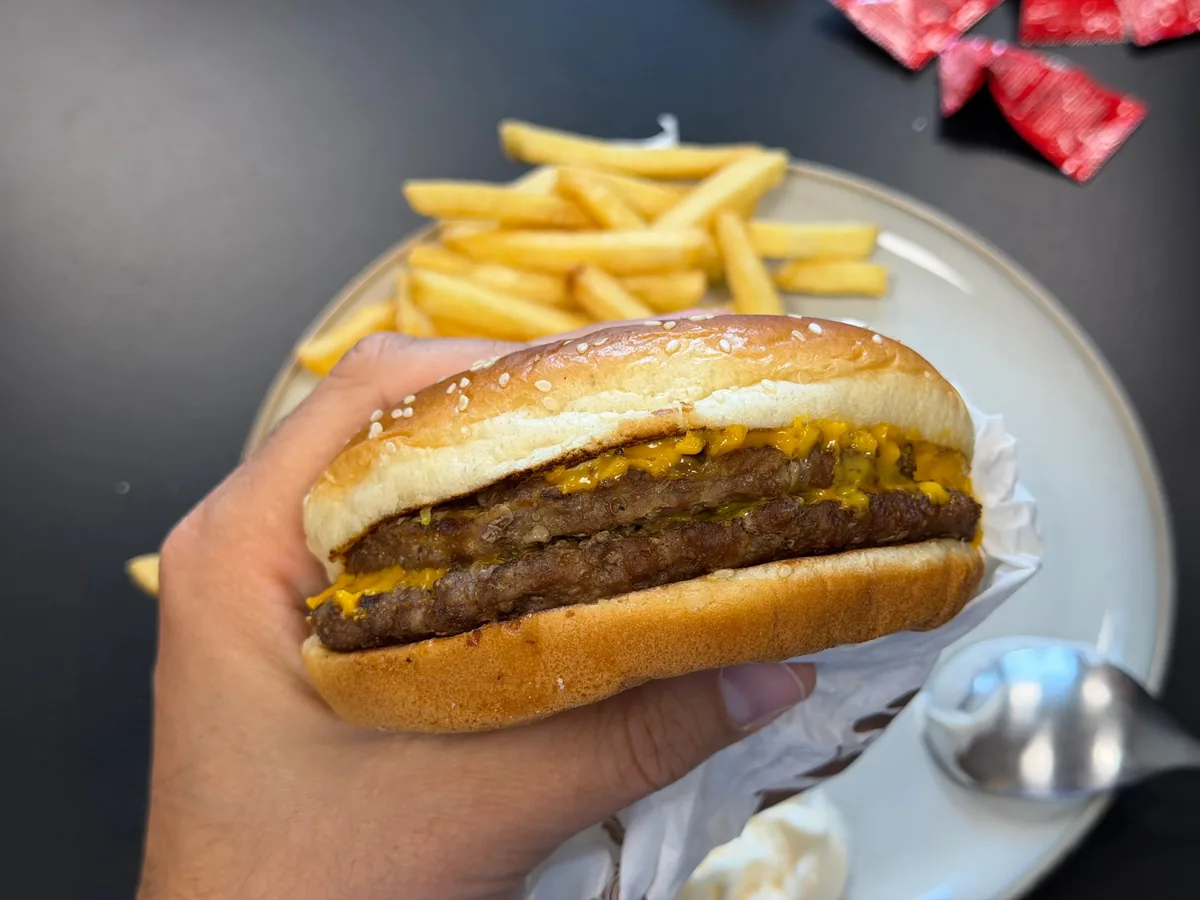 Double cheeseburger held in hand with french fries