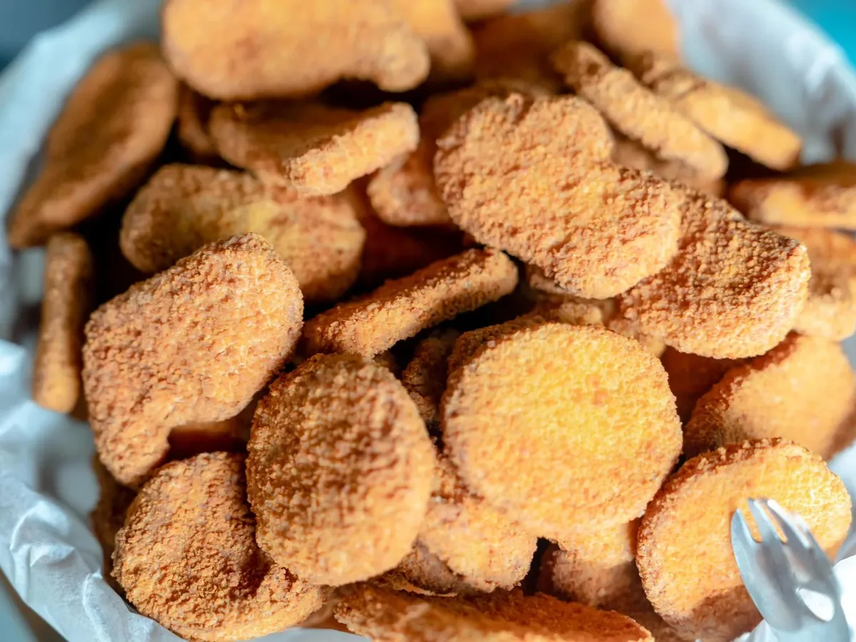 A pile of golden breaded chicken nuggets in a paper-lined basket with a fork.