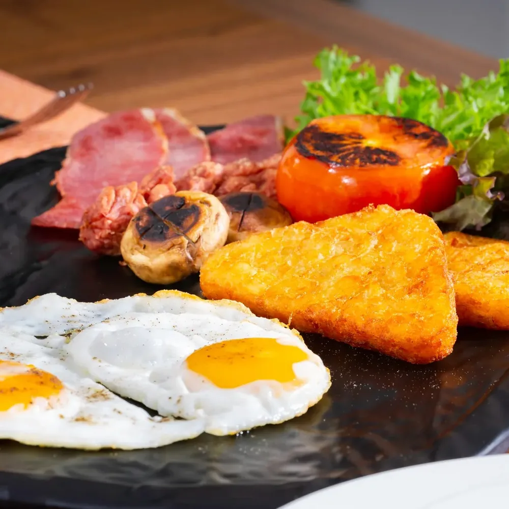 A breakfast plate with fried eggs, hash browns, grilled tomato, mushrooms, ham, and lettuce.