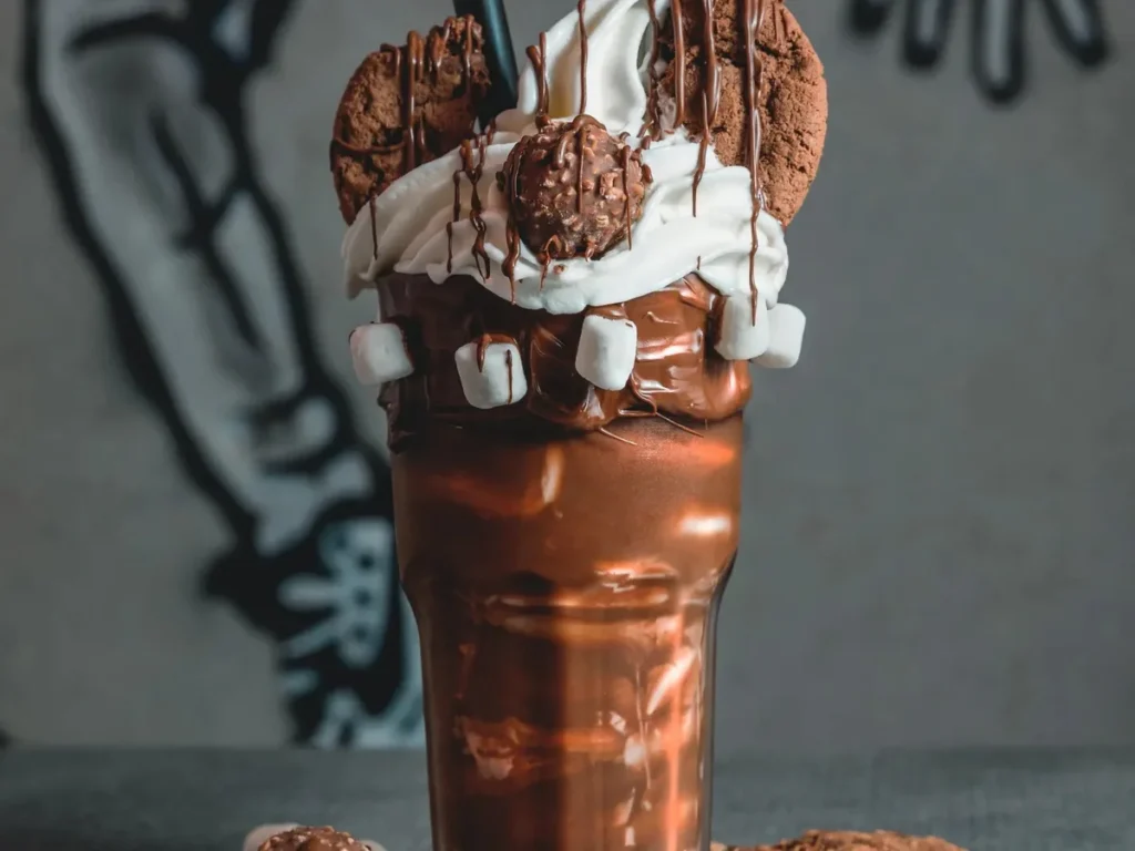 A chocolate milkshake topped with whipped cream, cookies, marshmallows, and chocolate drizzle.