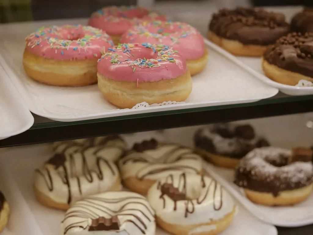 Doughnuts with pink, chocolate, and white icing arranged in a display case.