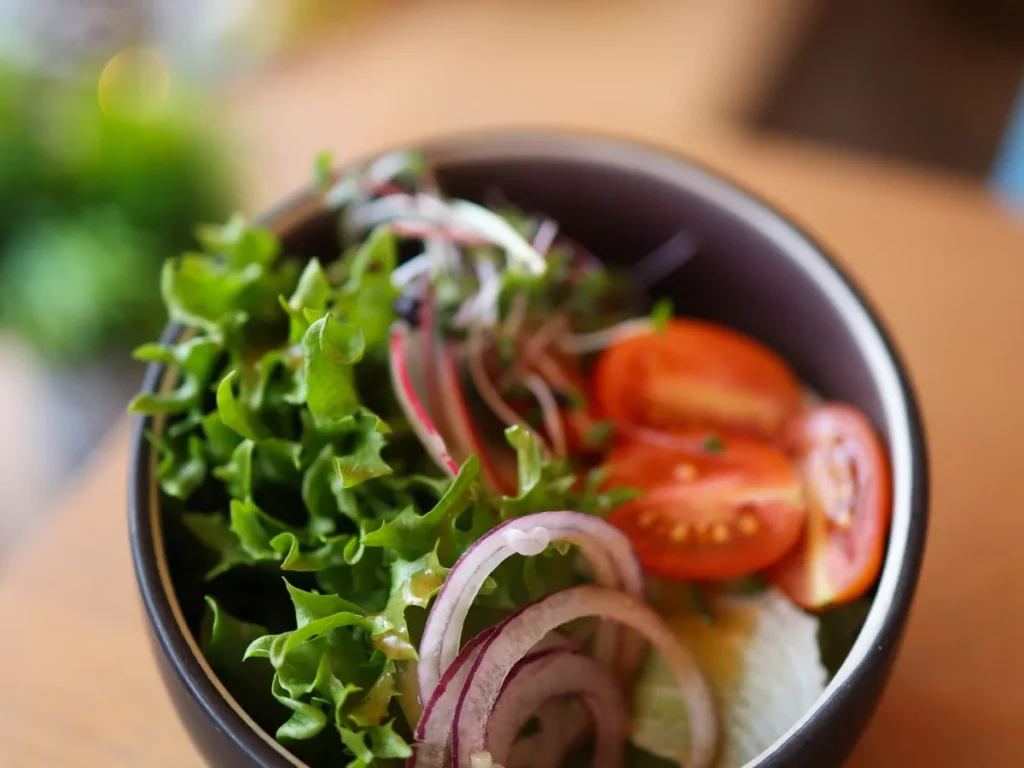 A fresh salad bowl with green lettuce, sliced tomatoes, and red onion rings.
