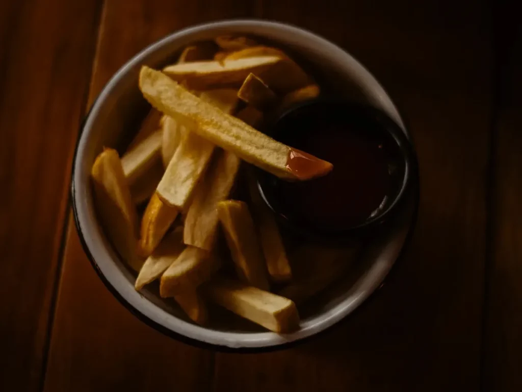Thick-cut French fries in a bowl beside a small dish of dipping sauce.