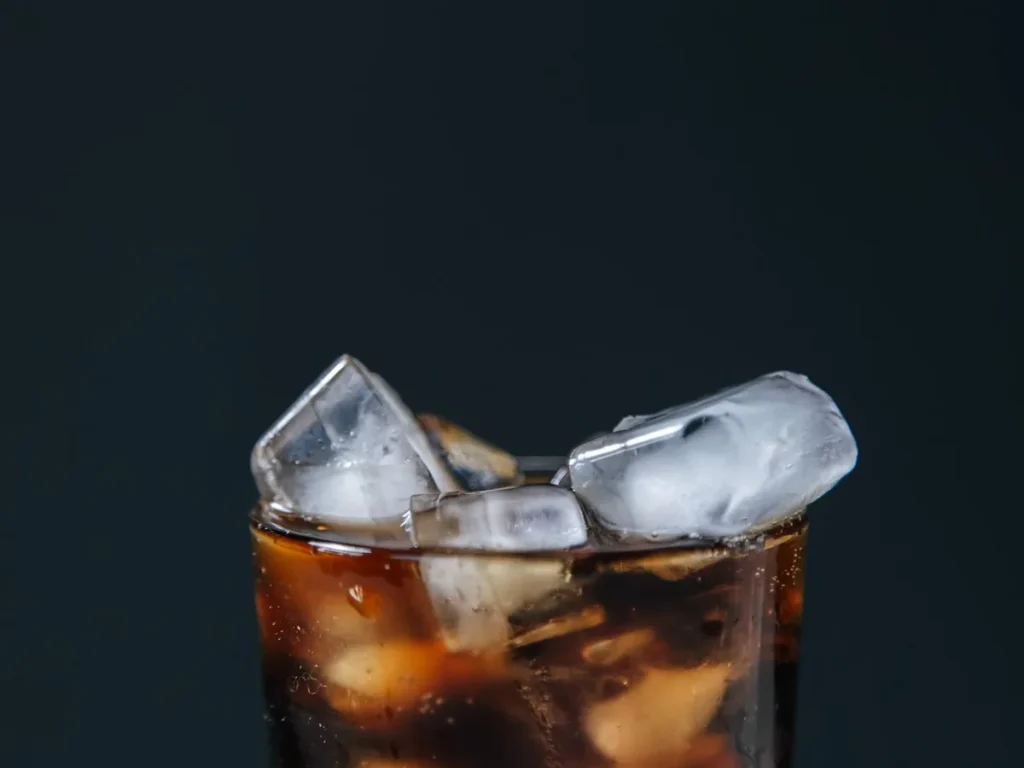 A glass of dark cola filled with ice cubes against a dark background.