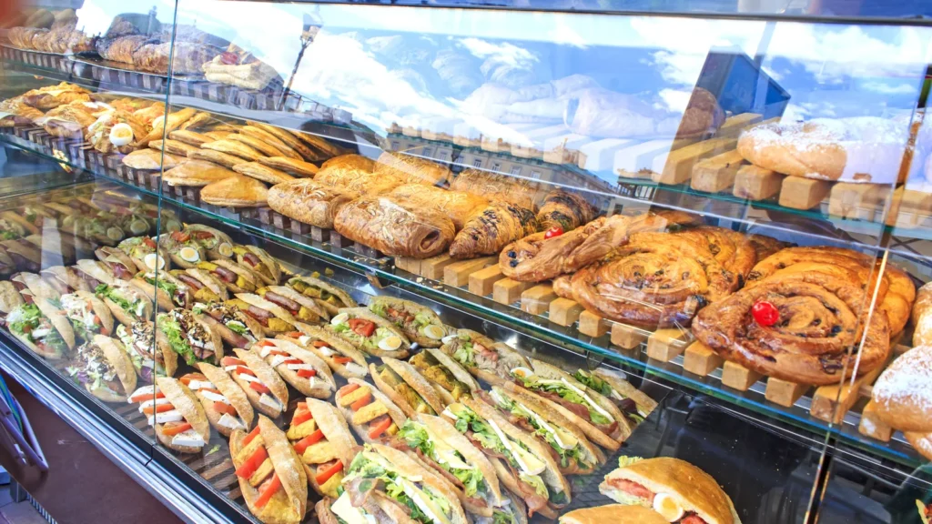 A glass display case filled with croissants, pastries, and filled sandwiches on wooden shelves.