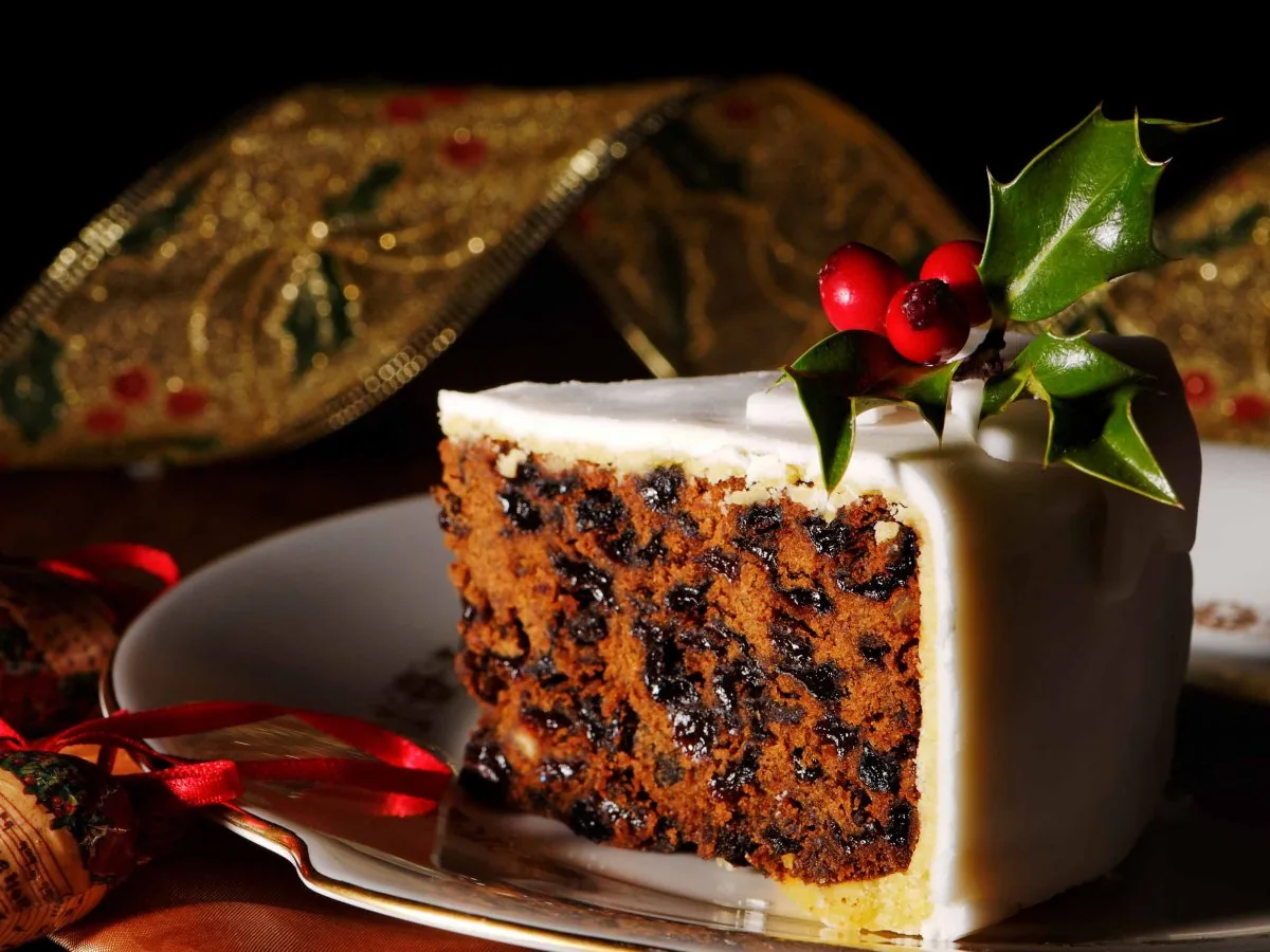 A slice of iced Christmas cake decorated with holly, served on a plate.