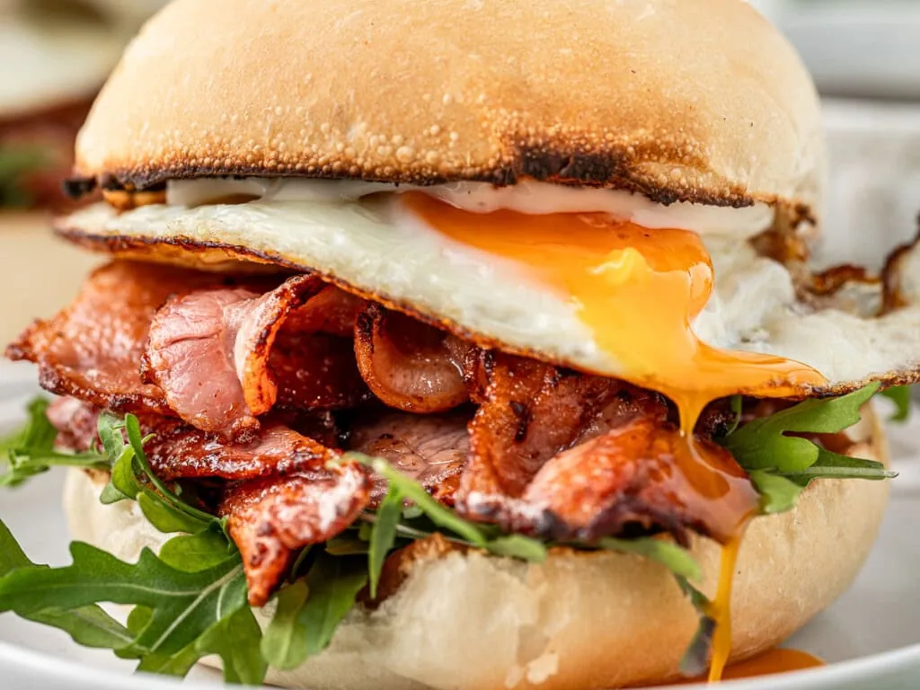 A breakfast roll filled with bacon and a fried egg with a runny yolk.