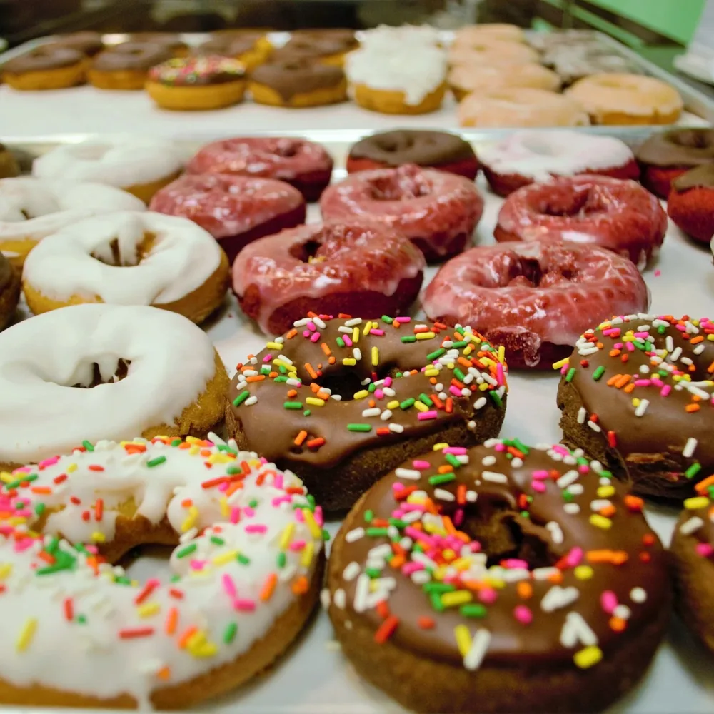 A tray of glazed doughnuts and sweet pastries with colourful toppings.