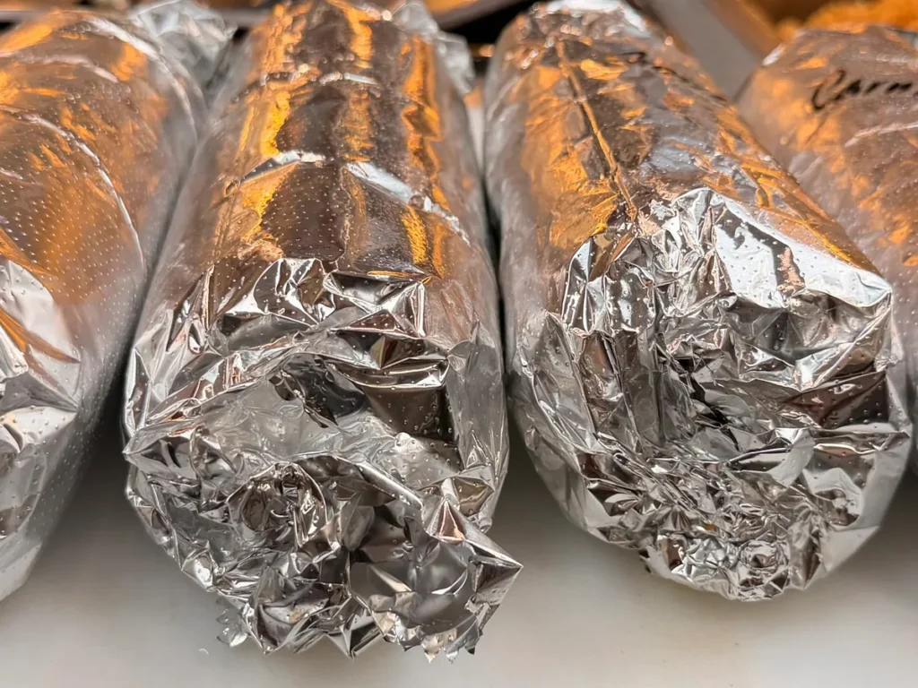 Several burritos wrapped in foil arranged in a row.