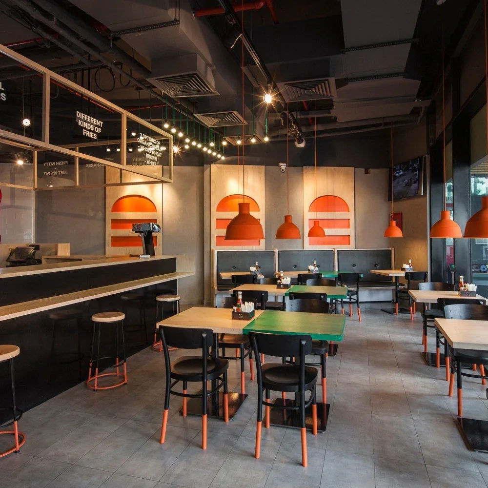 An empty restaurant dining room with tables, chairs, orange pendant lights, and a counter.