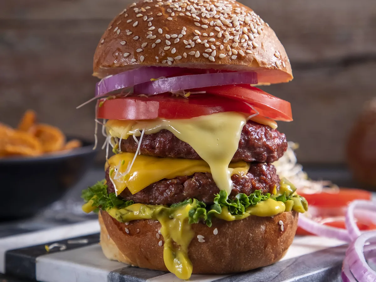 A double cheeseburger with melted cheese, tomato, red onion, and lettuce in a sesame bun.