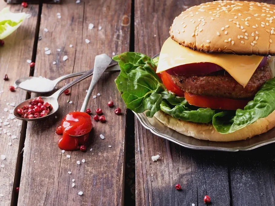 A cheeseburger with lettuce, tomato, and cheese in a sesame bun on a metal plate on a wooden table.