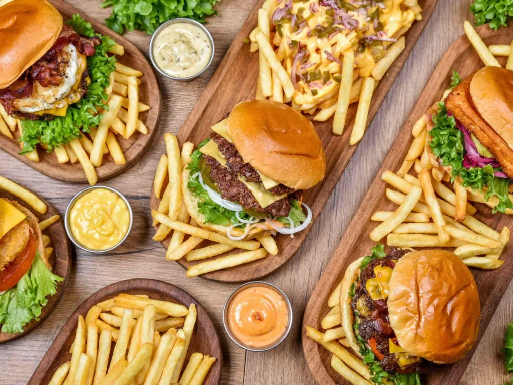 Several burgers with French fries and small bowls of dipping sauce arranged on wooden boards.