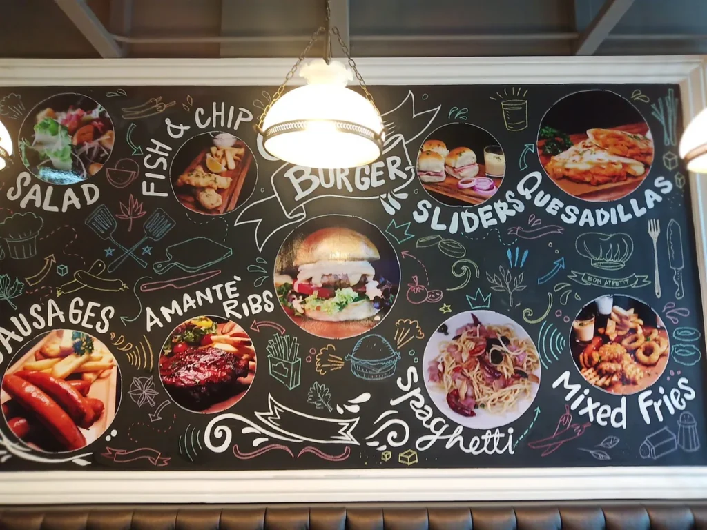 A dark chalkboard menu with dish names and circular food images, including a burger, salad, and fries.