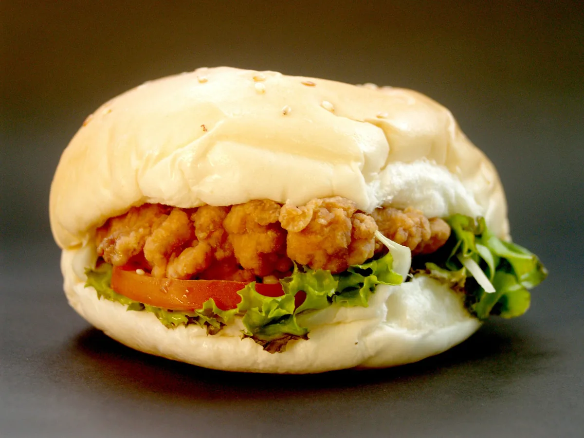 A fried chicken fillet burger with lettuce, tomato, and sauce in a soft bun.