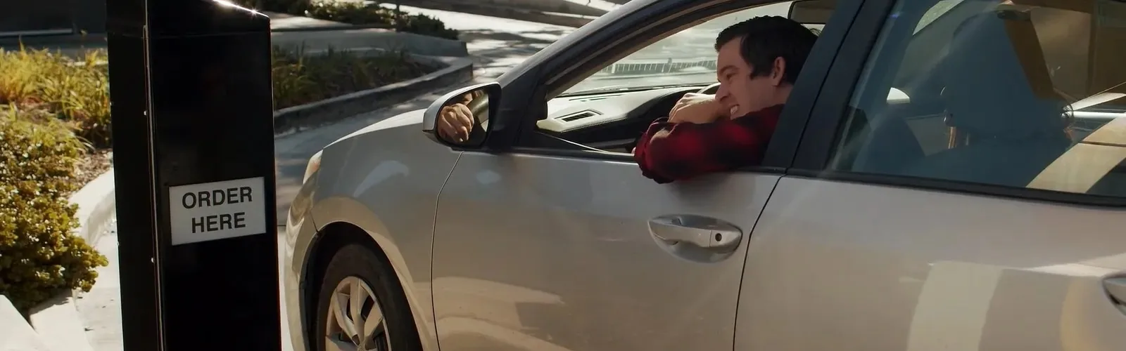 A driver leaning from a car window at a drive-through order point.