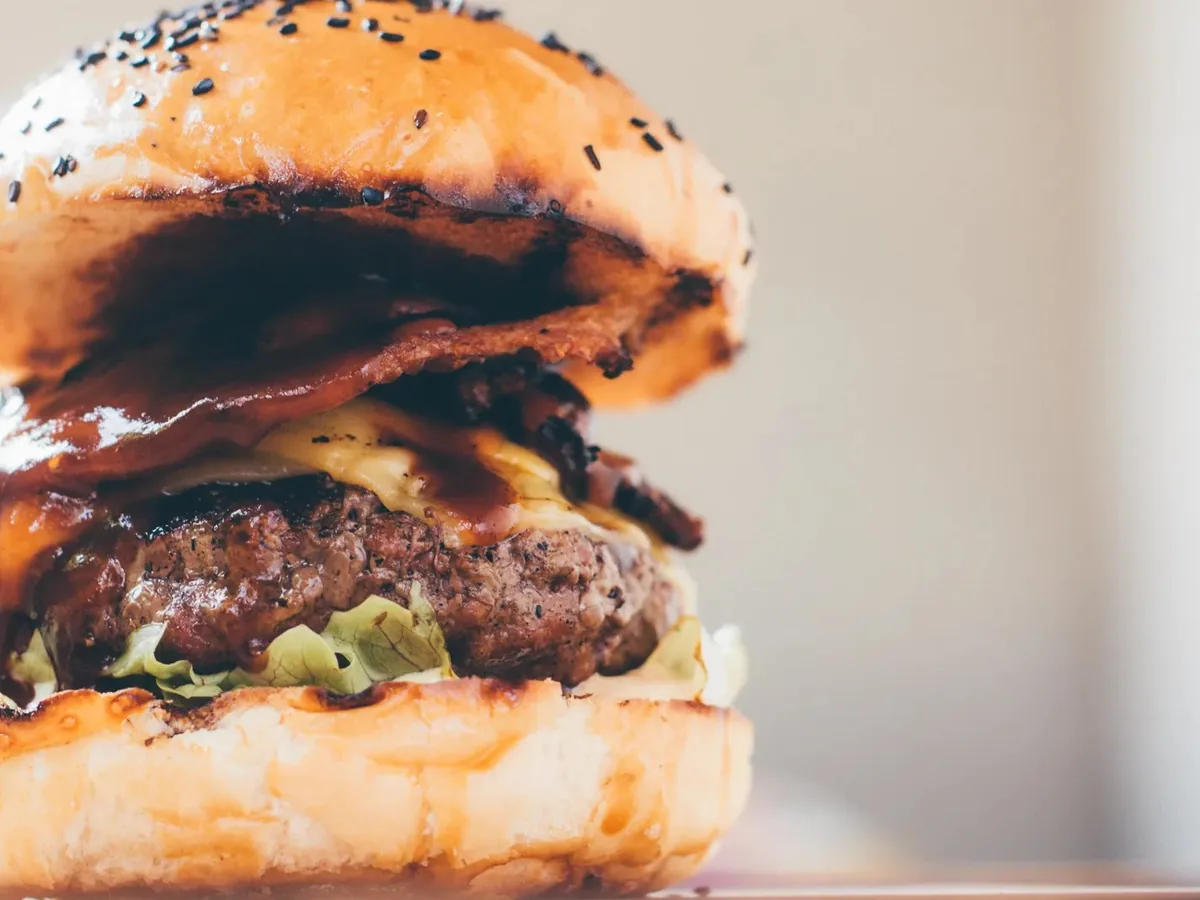A tall burger with a sesame seed bun, bacon, melted cheese, lettuce and sauce.