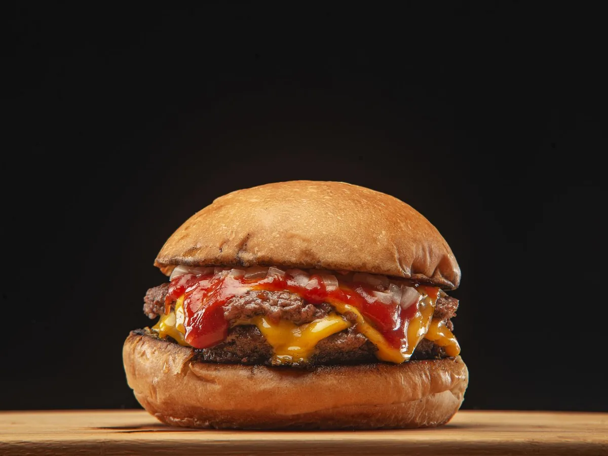 A double cheeseburger with melted cheese, ketchup and chopped onions on a wooden board.