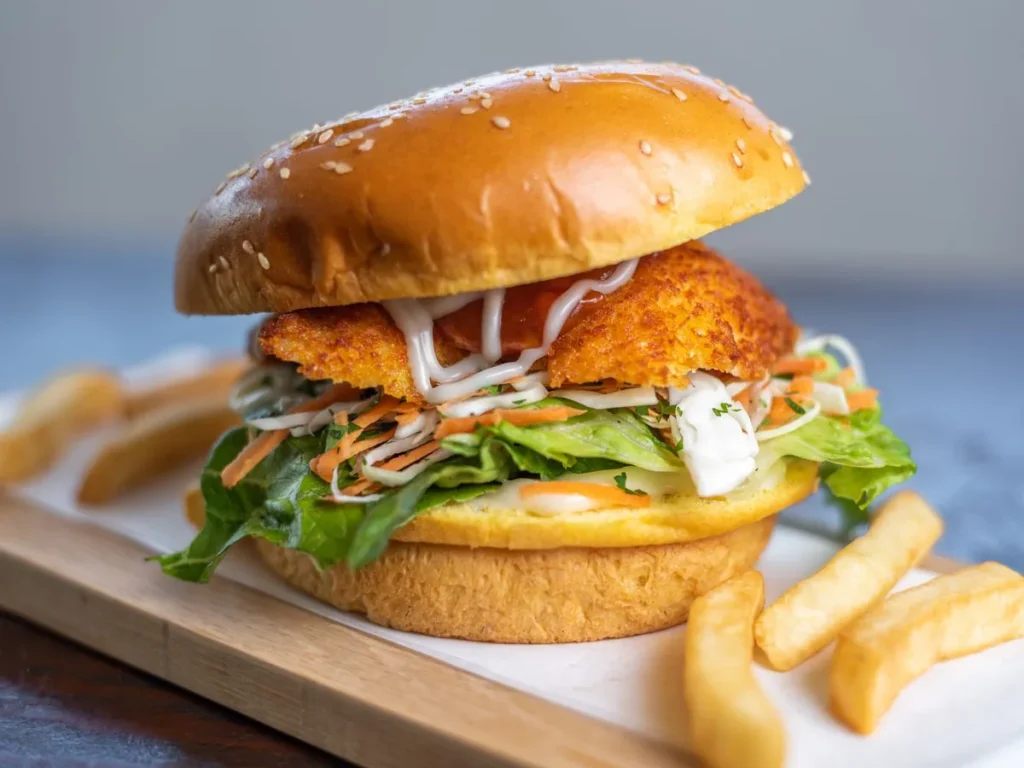 A breaded fillet burger with lettuce, shredded vegetables and sauce in a sesame bun, served with fries.