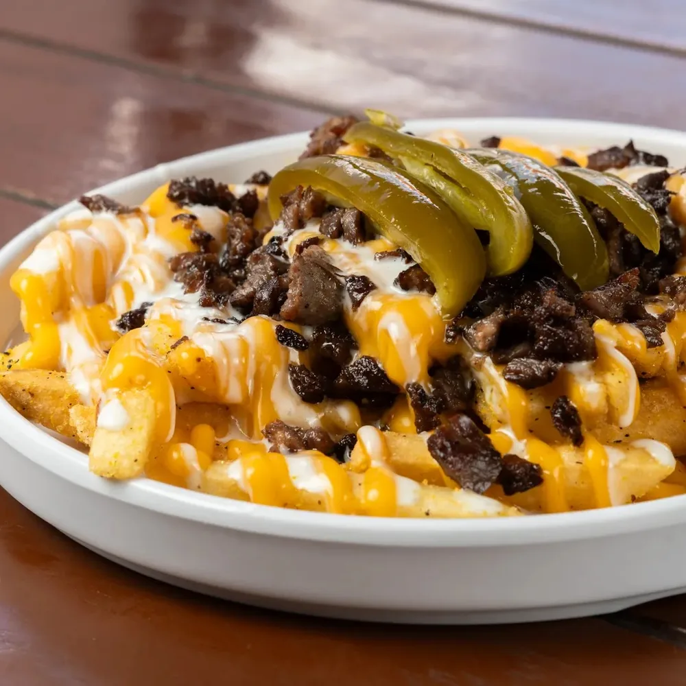 A bowl of loaded fries topped with melted cheese sauce, seasoned meat and pickled peppers.