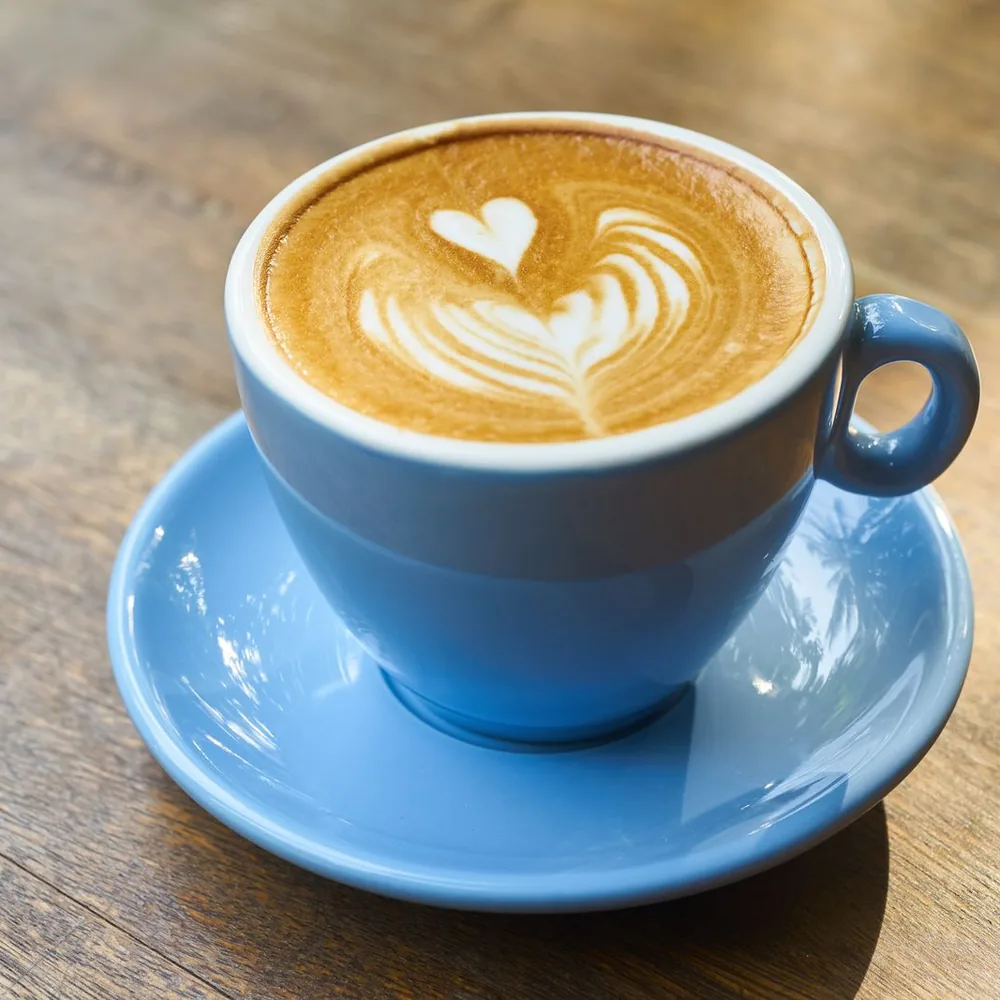 A blue cup of coffee with heart-shaped latte art on a matching saucer.