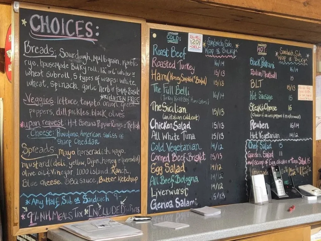 Large chalkboard menu boards listing sandwich choices, breads, vegetables, and spreads with prices above a counter.