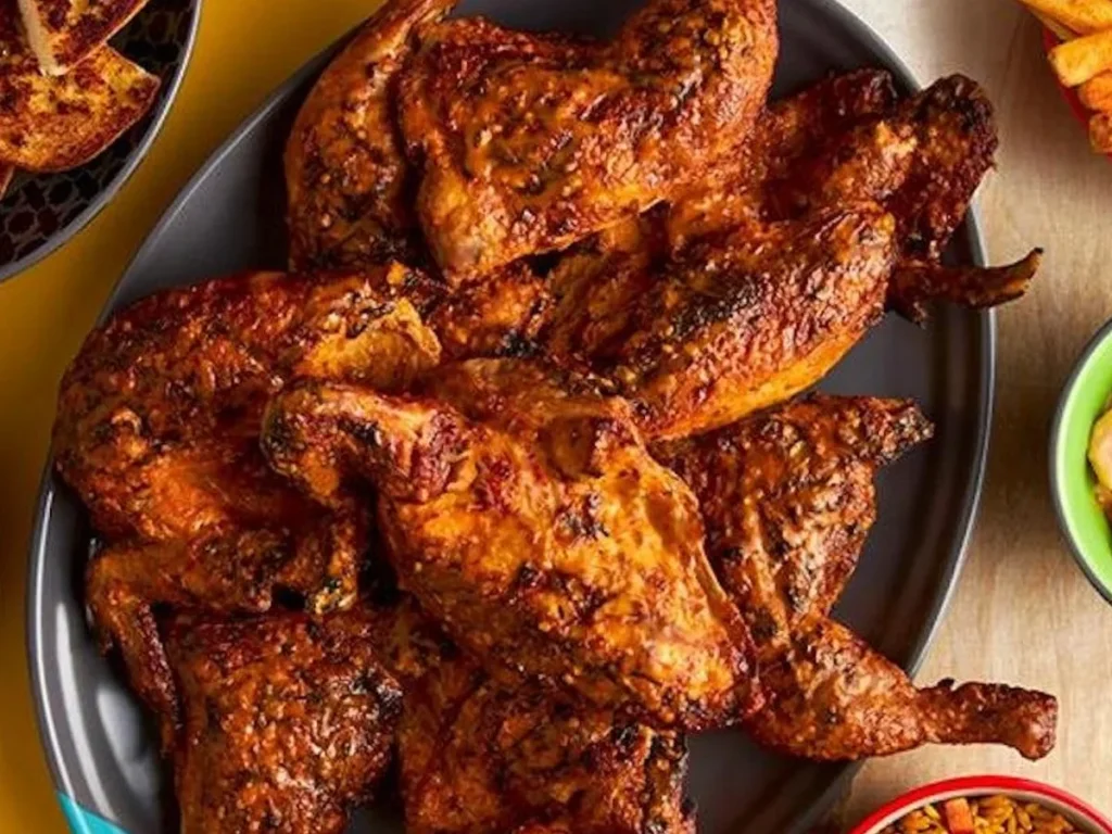 Flame-grilled chicken pieces piled on a plate, with side dishes at the edges of the table.