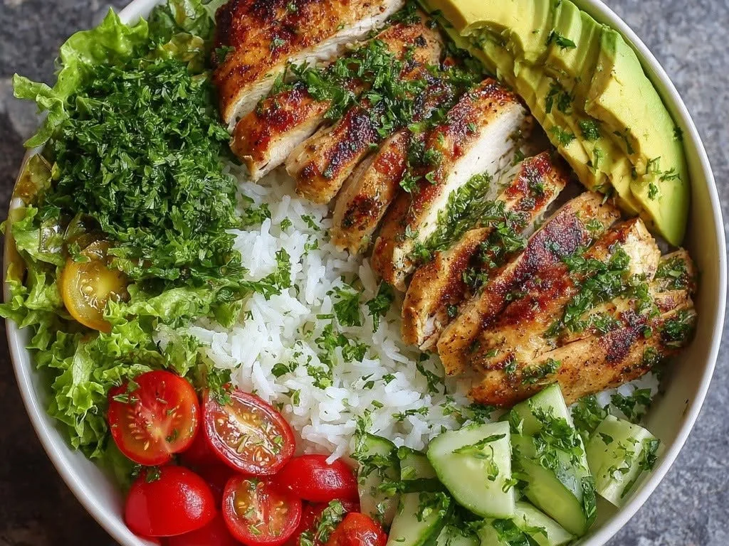 A bowl of sliced grilled chicken with rice, avocado, tomatoes, cucumber, and salad leaves.