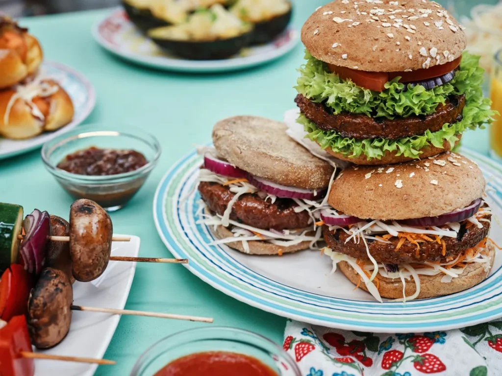 Vegetable burgers with lettuce, tomato, and onion on a plate, with grilled vegetable skewers beside them.
