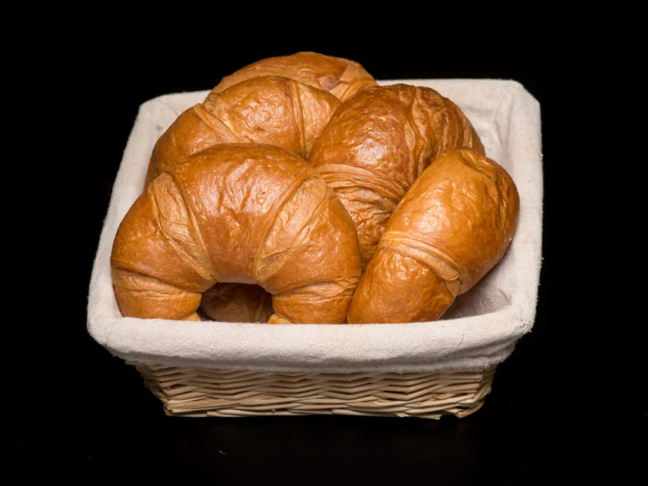 Golden baked croissants arranged in a cloth-lined basket.