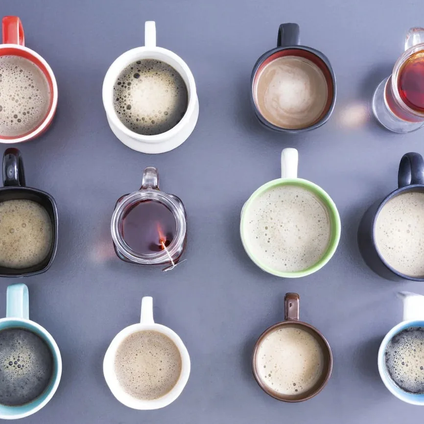 Several cups of hot coffee and tea arranged on a table, viewed from above.