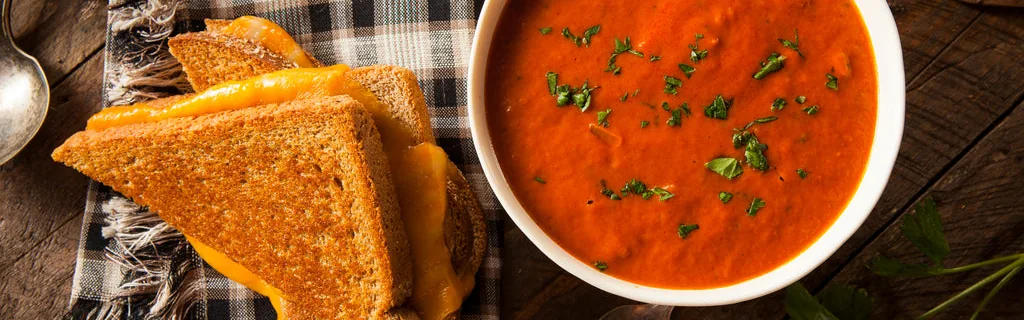 A bowl of tomato soup with herbs beside a toasted cheese sandwich.