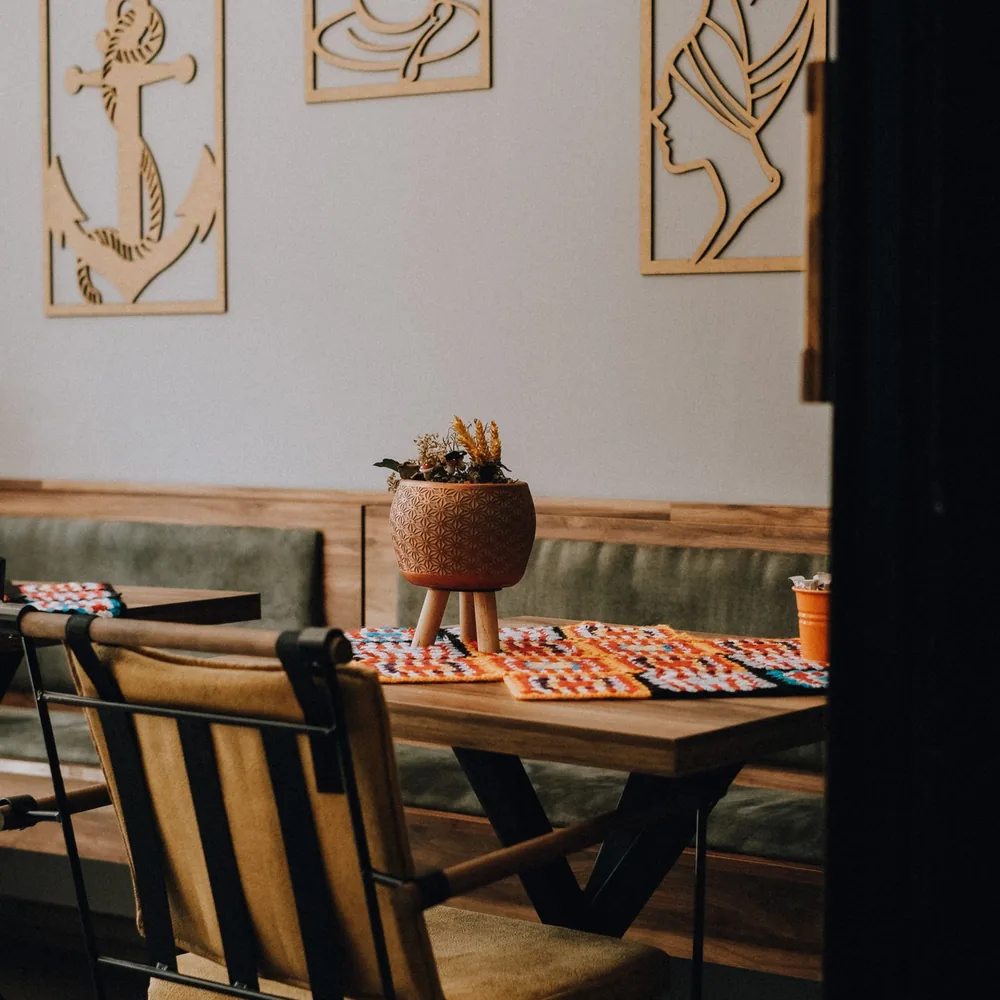A café seating area with a wooden table, colourful placemats, a potted plant and wall art.