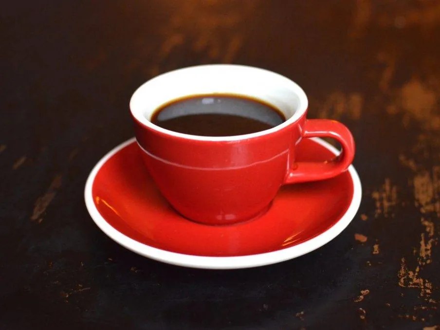 A red cup of black coffee on a matching saucer on a dark table.