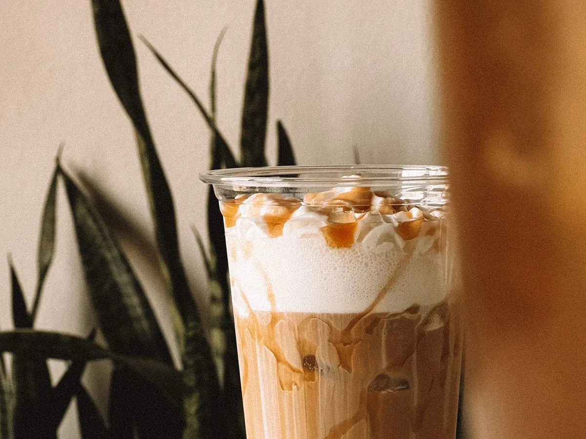 A blended iced coffee in a clear cup topped with whipped cream and caramel drizzle.